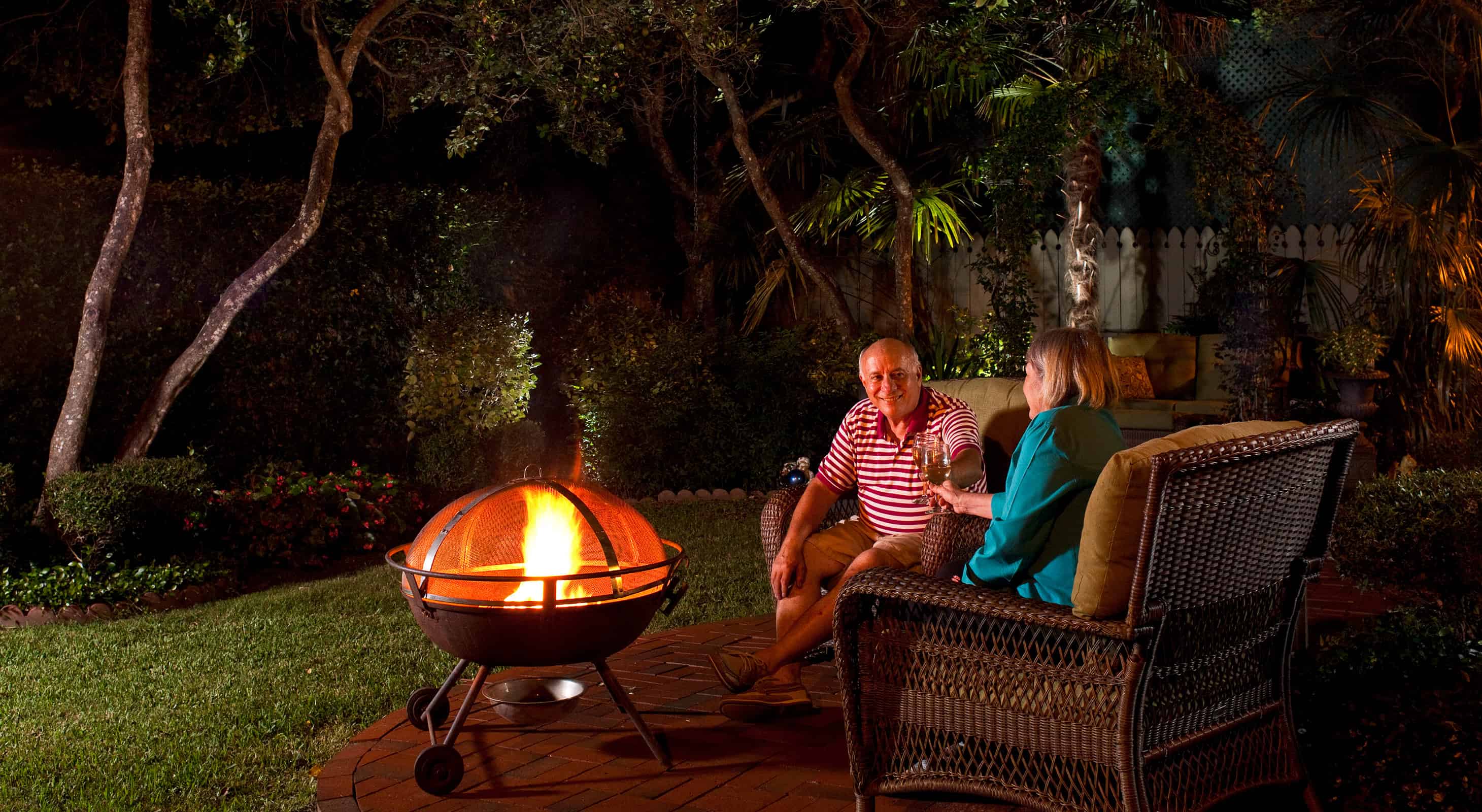 older couple with wine glasses sitting by a fire pit at night